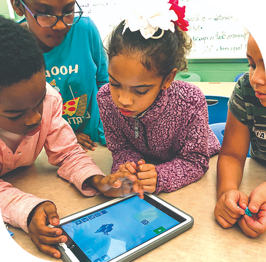 Children are gathered around a tablet, intently watching or interacting with it.