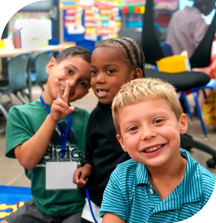 Young children are smiling and posing happily in a colorful classroom setting.
