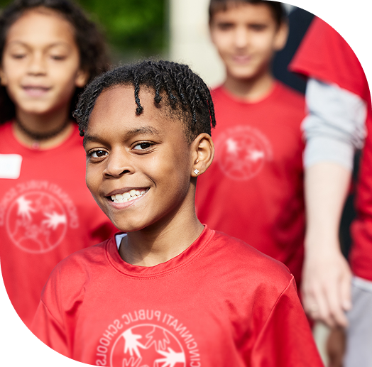A group of children wearing red shirts are smiling outdoors.